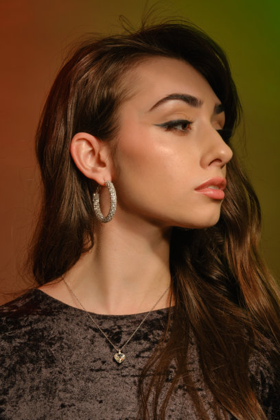 美丽的黑发女孩在时尚的珠宝和黑色天鹅绒连衣裙，在彩色背景下摆姿势。时尚和美丽。特写,复制空间图片下载