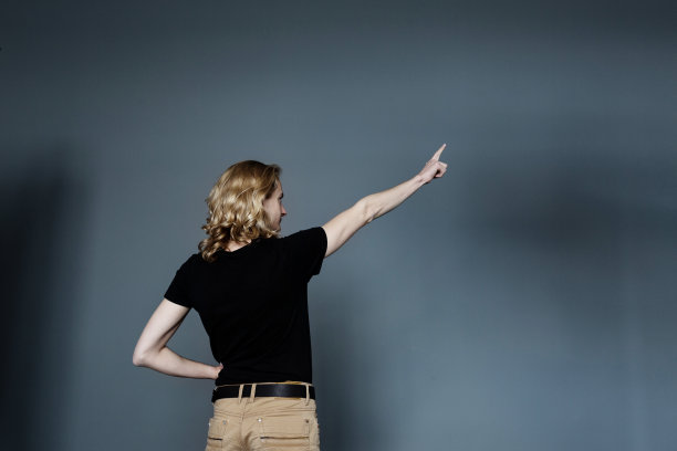 一位身穿黑色t恤和米色牛仔裤、身材瘦弱的年轻人竖着大拇指站在镜头前，一头金色长发。图片下载