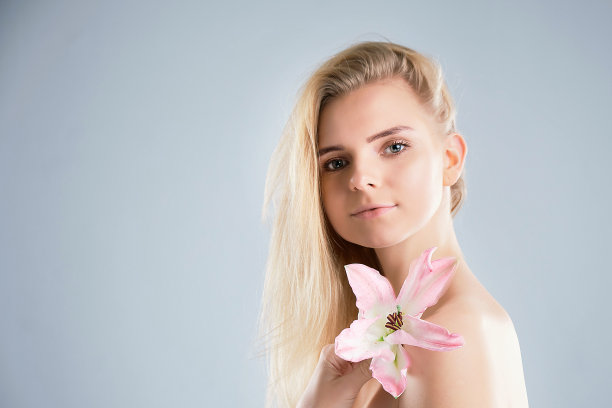 年轻女子与清洁新鲜的皮肤。年轻漂亮的女孩。照片中的金发女孩与莉莉在灰色的背景。皮肤护理的概念图片下载