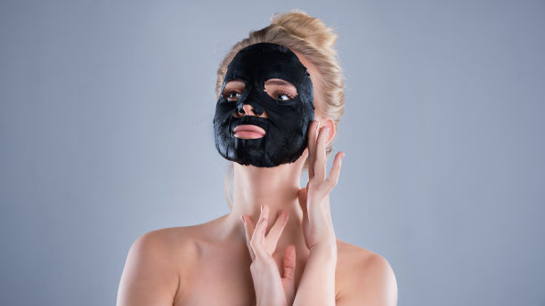 女孩裸肩摆姿势在灰色背景与面膜黑色，护肤概念，美容照片，皮肤治疗，保湿皮肤面膜，微笑。图片下载