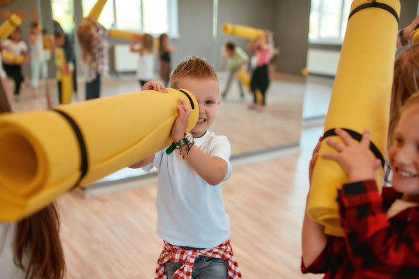 好玩的心情。在舞蹈室等待瑜伽课的时候，穿着休闲衣服的搞笑小男孩拿着一个黄色的垫子，从洞里往外看图片下载