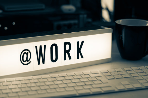 一个白色发光的电影院标志，上面写着黑色字母@WORK图片下载