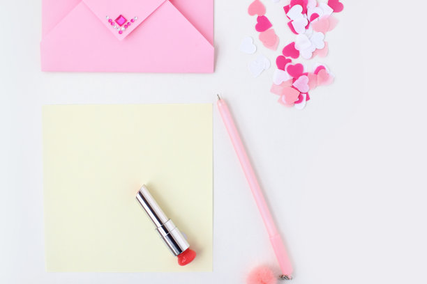 平铺:黄色的纸，粉红色的信封，上面有人造钻石，钢笔，绒球，口红，心形糖果。在信封里制作情人节明信片。做你自己。照片的图片下载