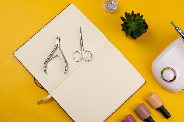 一套美容工具的美甲和足疗在一个橙色的背景。附近有一个打开的笔记本，用来写字，涂胶，磨指甲，剪刀和镊子图片下载