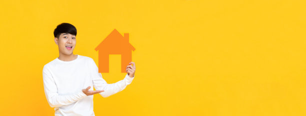 微笑英俊的亚洲男人在旗帜黄色的背景上举着房子标志图片下载
