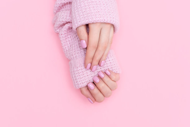 女性双手美甲近距离查看粉红色针织毛衣的背景。指甲画效果。美甲沙龙旗帜概念图片下载