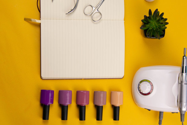 一套美容工具的美甲和足疗在一个橙色的背景。附近有一个打开的笔记本，用来写字，涂胶，磨指甲，剪刀和镊子图片下载