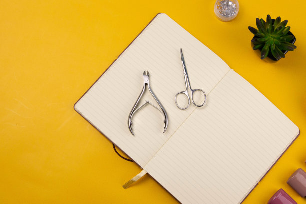 一套美容工具的美甲和足疗在一个橙色的背景。附近有一个打开的笔记本，用来写字，涂胶，磨指甲，剪刀和镊子图片下载