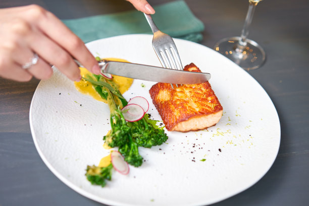 在一家餐厅的午餐，一位女士正在切鲑鱼排，并点缀着年轻的西兰花。餐厅菜单，一系列不同菜肴的照片图片下载