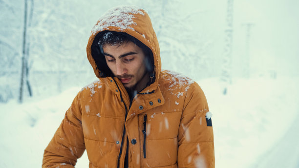 一个寒冷的人的肖像，穿着一件外套，在寒冷的雪地里捕捉雪花。图片下载
