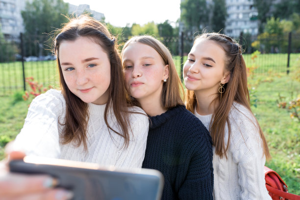 在城市里用手机拍照的三名少女（12-14岁），她们穿着休闲，笑容满面，在社交网络上分享照片图片下载