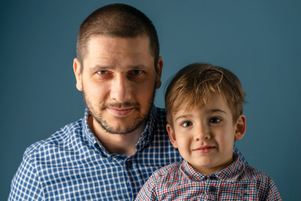 一个男人和一个男孩的肖像在蓝色墙壁前穿着屎白种人父亲和儿子摆姿势看着镜头图片下载