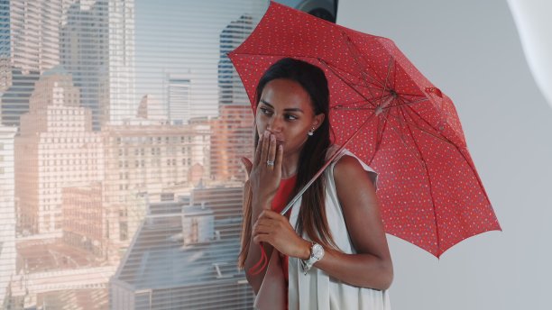 近距离微笑的黑色模特摆出红色伞在酒吧高椅子为时尚杂志拍摄照片图片下载