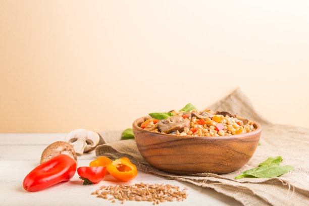 斯匹尔特小麦粥与蔬菜和蘑菇木碗在白色和橙色的背景和亚麻纺织品。侧视图，选择性聚焦，复制空间。图片下载