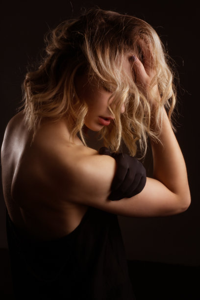 深色背景中，身穿深色连衣裙、用黑色丝带遮住眼睛的金发女郎的棚拍肖像图片下载