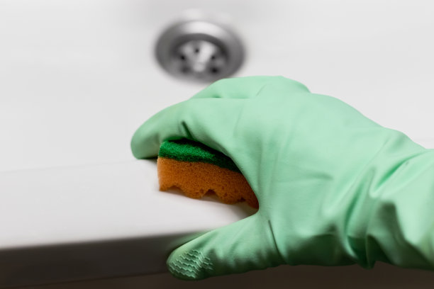 戴薄荷绿橡胶手套的手用橙色海绵擦拭白色浴缸或水槽的表面，在现代浴室清洁图片下载