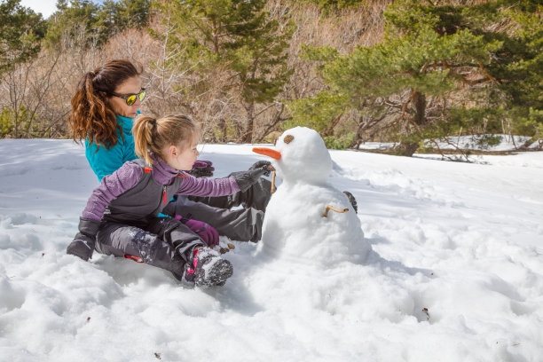 女人和小女孩坐在大自然中堆雪人图片下载