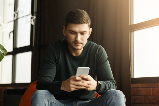 坐在室内豆袋椅上用智能手机发短信的千禧一代图片下载