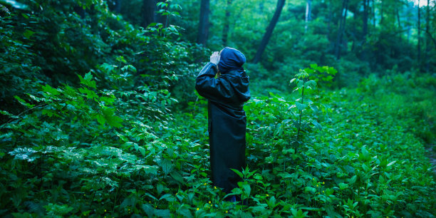 穿着雨衣的男人在潮湿的森林背景。绿色的夏天自然。感觉孤独。人们穿着雨衣旅行。雨在森林。穿着湿雨衣的年轻游客。自然全景。寂寞的人的轮廓图片下载