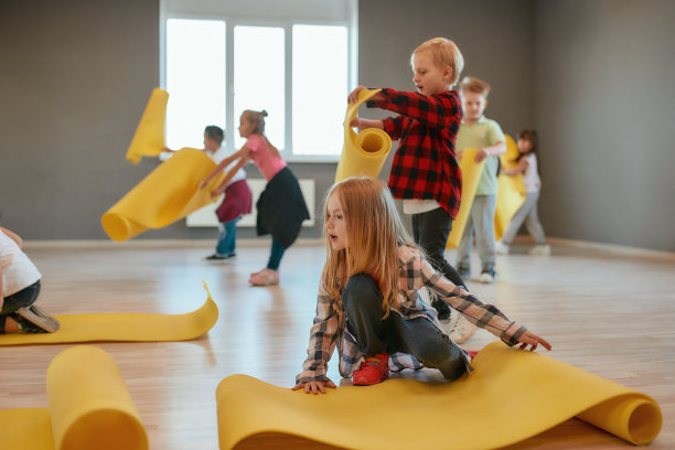 体操课。一群可爱的孩子穿着休闲服在地板上放着黄色的垫子，准备上瑜伽课图片下载