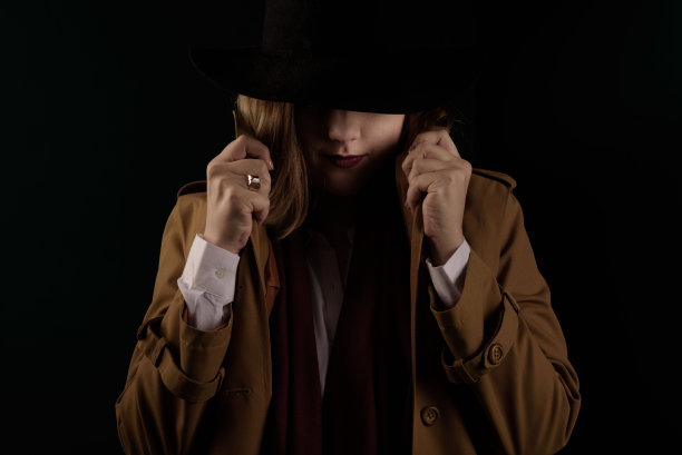 穿着棕色斗篷，戴着黑色帽子的复古黑帮女。按照黑手党的风格拍照。暗模糊的背景，图像焦点在帧的顶部移位。图片下载