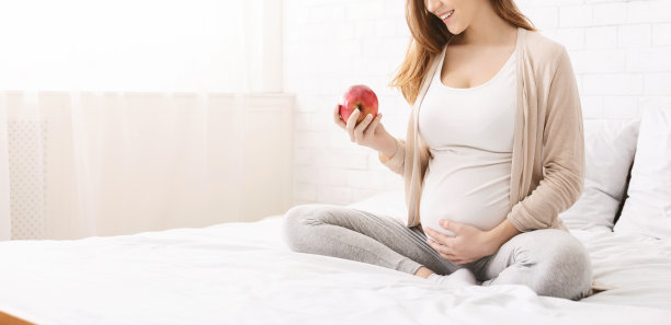 孕妇坐在床上吃有机红苹果图片下载