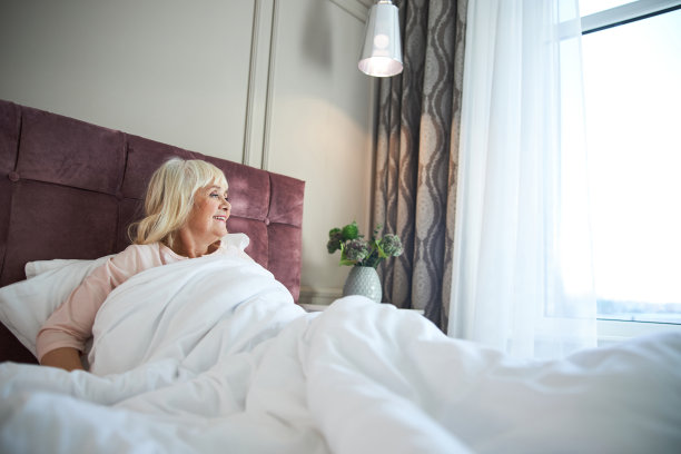 微笑的成年妇女坐在家里的床上图片下载