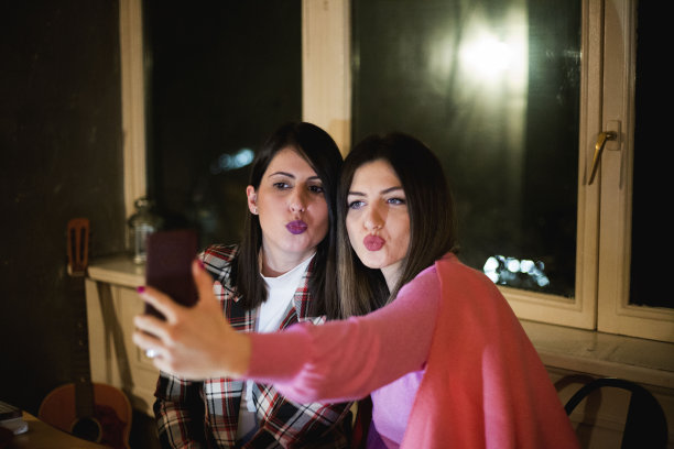 快乐的年轻女子在咖啡馆自拍。两个迷人的女性朋友微笑使完美的照片在一起。技术概念图片下载