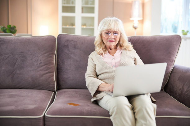 微笑的老妇人在家里使用笔记本电脑图片下载