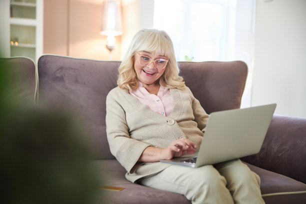 在房间里用笔记本电脑打字的快乐老太太图片下载