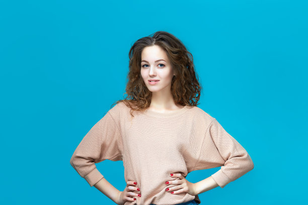 一个年轻美丽的女人的肖像穿着运动衫手拉手的臀部孤立在蓝色的背景图片下载