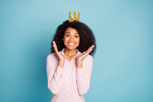 照片惊人的黑皮肤女士高兴地被公认为舞会皇后难以置信的情绪穿金色皇冠粉红色衬衫孤立的蓝色背景图片下载