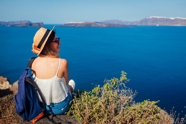 希腊圣托里岛阿克罗蒂里的女游客坐在岩石边缘观看爱琴海的火山口。旅游图片下载