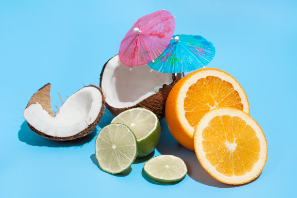 新鲜多汁的橙子，椰子和青柠与鸡尾酒伞孤立在蓝色的背景。健康饮食和节食的概念。旅游和度假概念图片下载