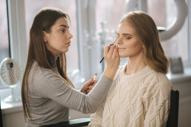 化妆师在她的美容工作室工作。女性肖像由专业化妆师涂抹。美丽的化妆师开始为金发模特化妆图片下载