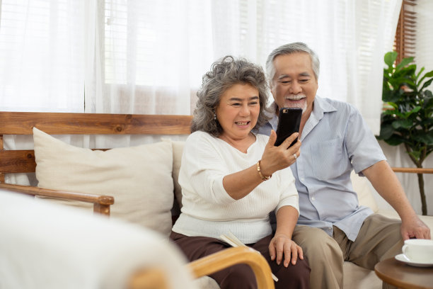 快乐的亚洲夫妇坐在沙发上，一起使用智能手机与家人视频聊天或自拍，享受科技带来的沟通和退休生活图片下载