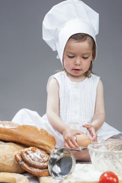 穿着特定厨师制服的白人女孩在厨房玻璃器皿中分解新鲜鸡蛋并制作食物，在工作室环境中使用搅拌器。灰色背景。竖版照片图片下载