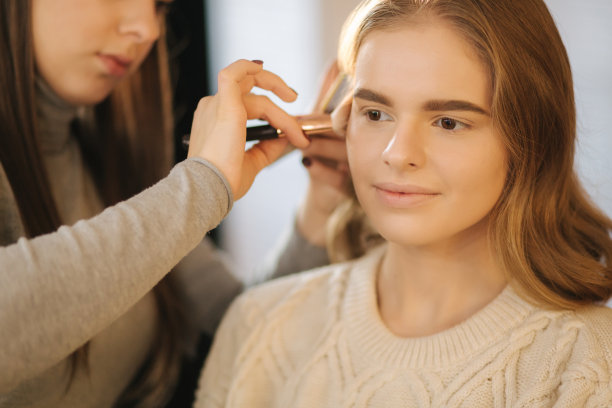 化妆师在她的美容工作室工作。女性肖像由专业化妆师涂抹。美丽的化妆师开始为金发模特化妆图片下载