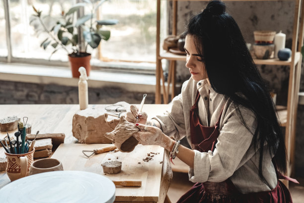 工匠概念：年轻女子在室内制作陶器，用工具塑造粘土图片下载