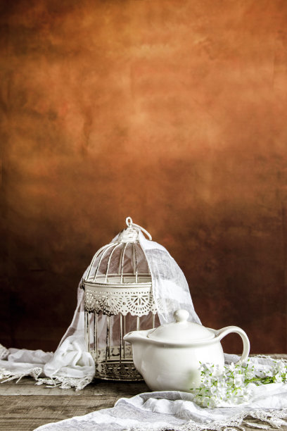 木桌上放着一个白色的笼子和一个带花和装饰的茶壶图片下载