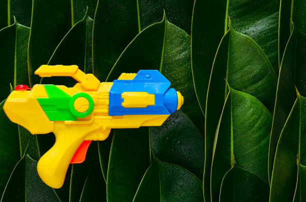 黄色的水枪放在绿色的树叶上，为泼水节或泼水节作背景图片下载