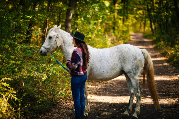 年轻的模特马术妇女走在秋天的树林与马图片下载