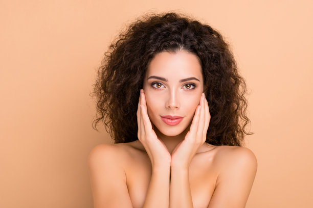 近距离的照片美丽惊人的她，她的模特涂抹，触摸面部皮肤，健康的卷发，发型，理想的外观，丰满诱人，大嘴唇，不穿衣服，，孤立的米黄色，柔和的背景图片下载