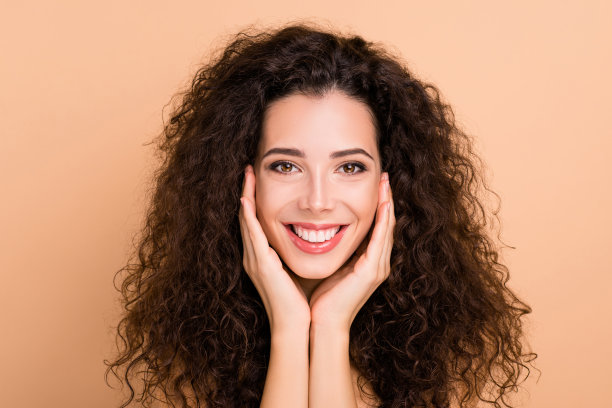 近距离的照片美丽惊人的她，她的模特涂抹，触摸面部皮肤，健康的卷发，发型，理想的外观，丰满诱人，大嘴唇，不穿衣服，，孤立的米黄色，柔和的背景图片下载