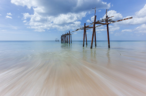 古老的木桥和海滩上的海浪在阳光灿烂的天空背景在皮莱海滩，攀牙，泰国图片下载