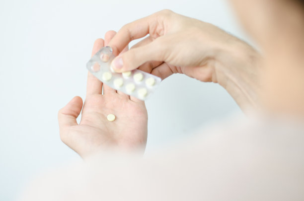 一个圆形药丸在年轻男性的手的特写照片。人用一杯水吃药。每日规范维生素、有效药物、现代医药对身心健康的理念。图片下载