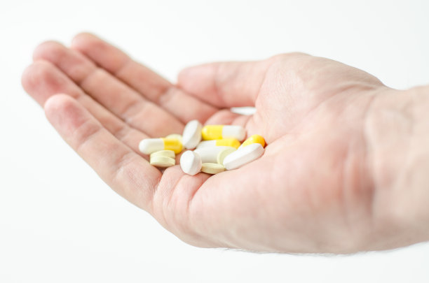 一个圆形药丸在年轻男性的手的特写照片。人用一杯水吃药。每日规范维生素、有效药物、现代医药对身心健康的理念。图片下载