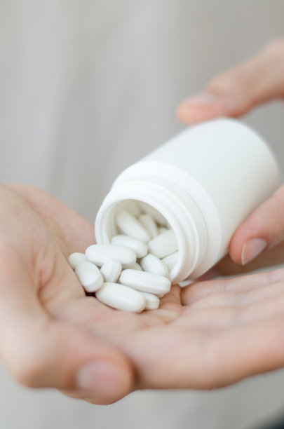 一个圆形药丸在年轻男性的手的特写照片。人用一杯水吃药。每日规范维生素、有效药物、现代医药对身心健康的理念。图片下载