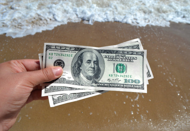 女孩手持300美元钞票，背景是海浪图片下载