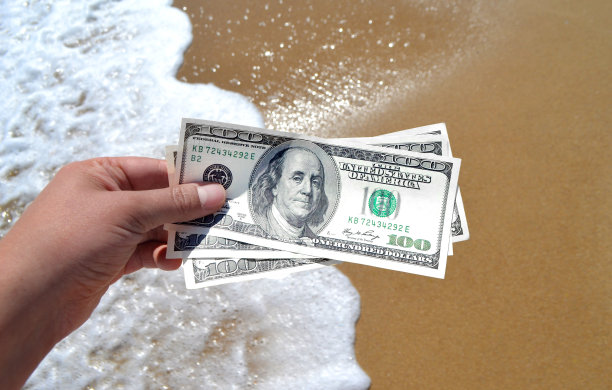 女孩手持300美元钞票，背景是海浪图片下载